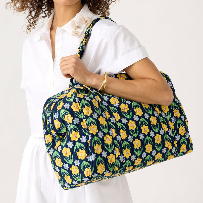 model wearing white dress and holding weekend travel bag with floral print