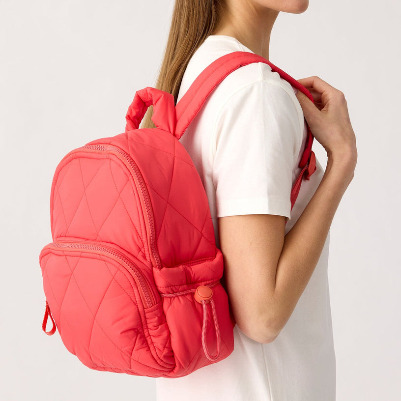 model with small bright coral pink quilted backpack over the shoulder