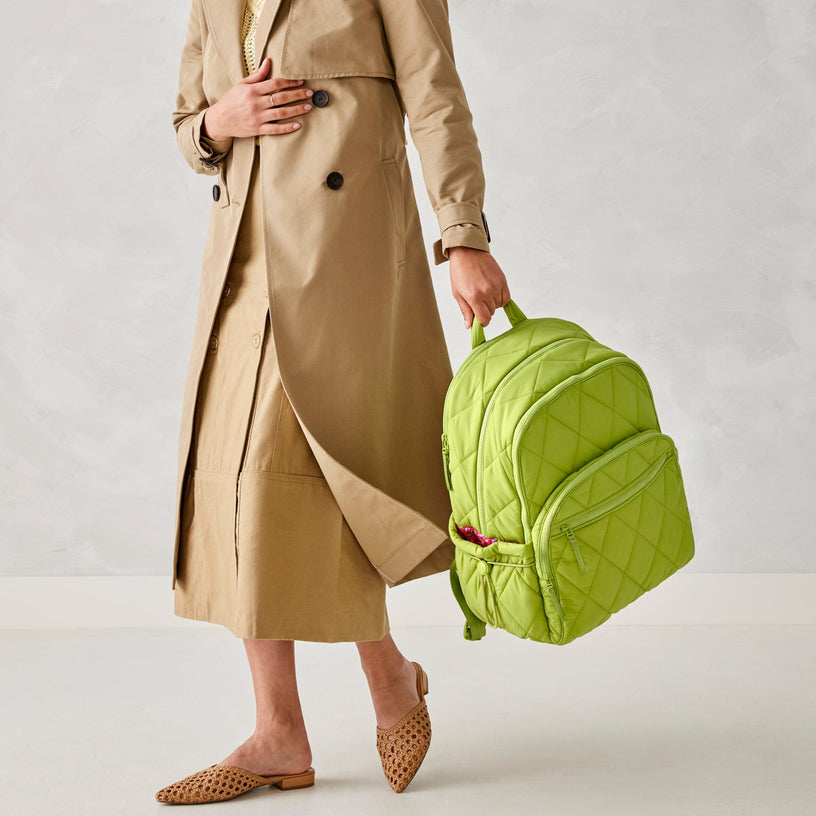 model wearing long beige trenchcoat and carrying a large bright green quilted backpack