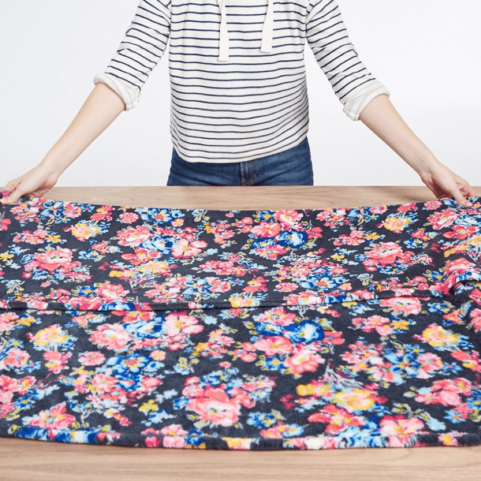 Person folding a floral fleece blanket in half lengthwise